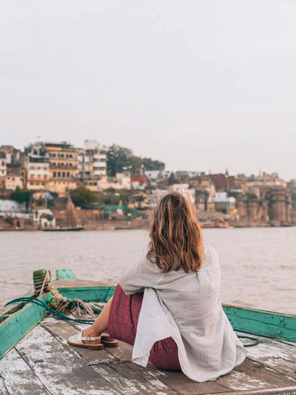 Lost in the search for peace, she found herself. A portrait from behind, showing a traveler soaking in the panoramic view of the Banaras ghats from a boat.