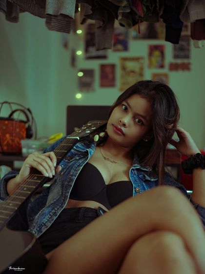 A lifestyle portrait in a room, using props like a guitar to tell a story about the subject's personality. The lighting is designed to feel natural and relaxed.