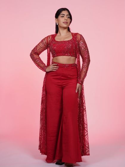 A full-length view of our red three-piece Indo-Western set. The sparkling sheer jacket over the crop top and pants is a modern power look.
