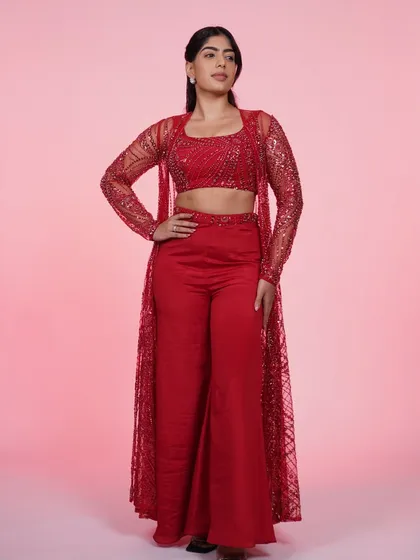 A full-length view of our red three-piece Indo-Western set. The sparkling sheer jacket over the crop top and pants is a modern power look.