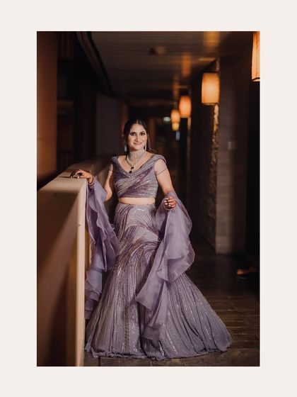 The bride in her flowing lavender lehenga, posing in a softly lit corridor. A portrait of modern elegance and style.
