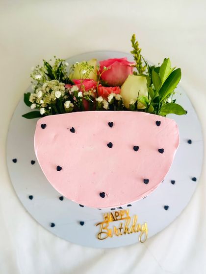 A sweet and simple half-and-half cake design, with one side covered in pink frosting with black hearts and the other topped with fresh flowers.