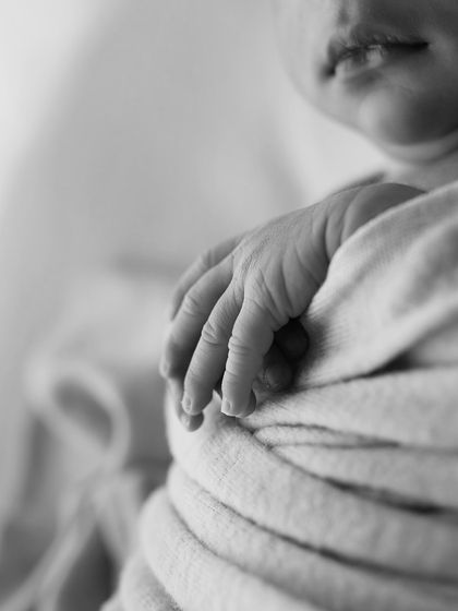 A close-up of a newborn's tiny, wrinkled hand in black and white. This macro shot preserves one of the most unforgettable details of the newborn phase.