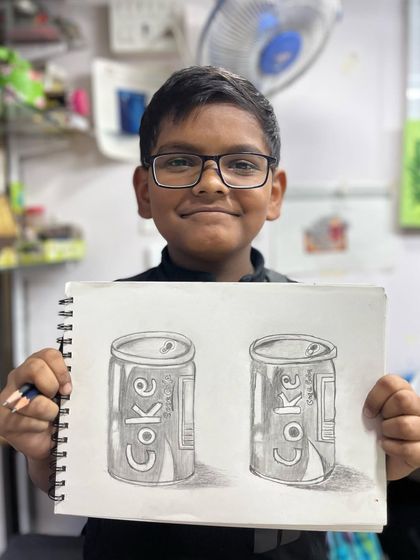 Fantastic progress after just six sessions. This 9 year old student proudly shows his pencil shading study of Coke cans, where he learned to create form and texture.