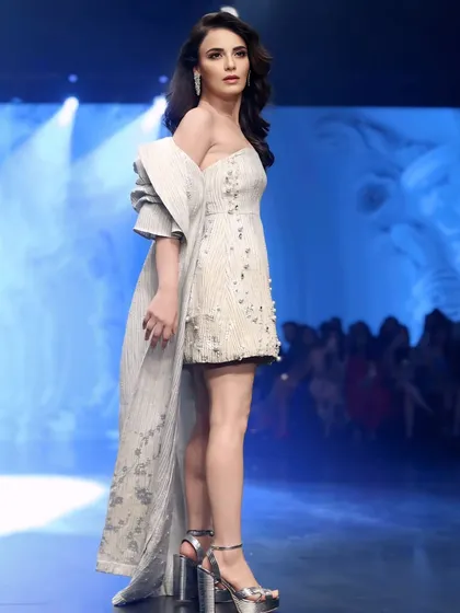 A side profile of Radhika Madan on the ramp, showcasing the elegant silhouette of her white dress and long cape.