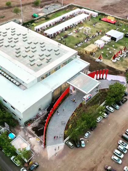 An aerial view of the Glass Pavilion, showing the main building, the curved entrance pathway, and the adjacent parking and event grounds.