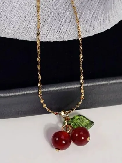 A playful and cute cherry charm necklace. The red cherry beads and green leaf are a fun pop of color on a shimmering gold-tone chain.