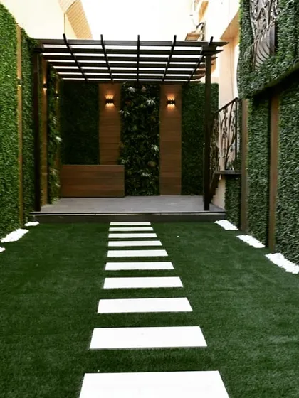 A narrow walkway transformed into a striking entryway. The path is flanked by tall artificial green walls and leads to a raised deck with a pergola, creating a dramatic sense of arrival.