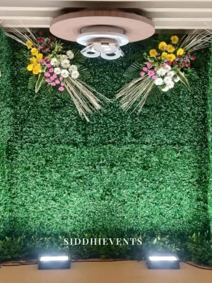 A lush, green-themed backdrop made of a dense foliage wall, accented with bouquets of colorful flowers, creating a serene, garden-like atmosphere indoors.