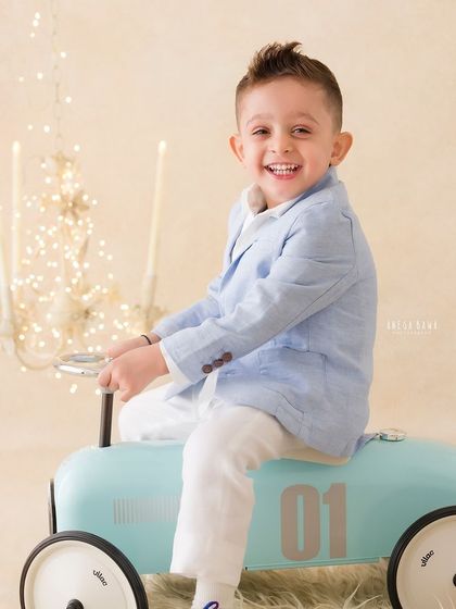 A candid shot of a little boy laughing with joy as he plays on a toy car during his photoshoot.