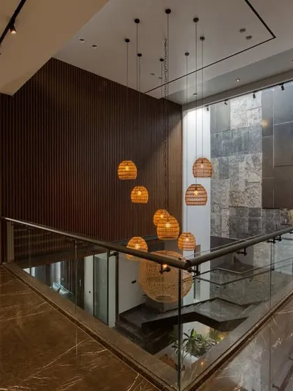Looking down from the upper floor of a residence, this view highlights the double-height space, the rich marble flooring, and the warm glow of the cascading wicker light fixtures.