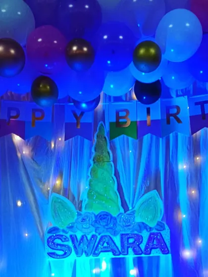 A unicorn-themed backdrop illuminated with blue light, creating a mystical and magical atmosphere for Swara's birthday celebration.