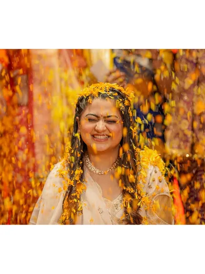 A moment of pure bliss. The bride closes her eyes and smiles as she is showered with marigold petals, a perfect, candid shot of Haldi happiness.