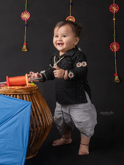 A playful shot of a baby boy enjoying the Makar Sankranti props. The traditional black kurta with embroidery adds an authentic touch to the festival theme.