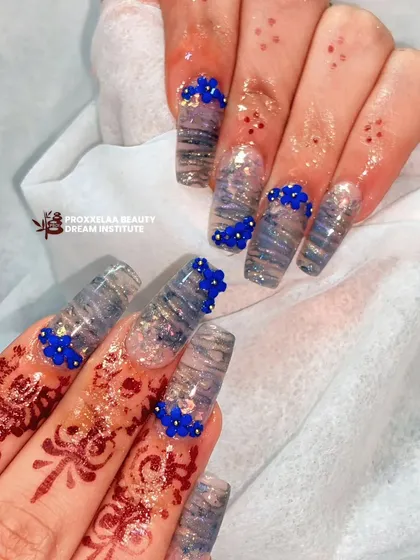This design combines a translucent, wavy pattern with clusters of tiny, hand-sculpted blue flowers. The 3D floral details add a pop of color and texture to these long, square extensions.