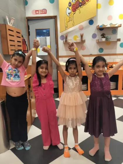Four friends celebrating a birthday, holding hands with arms raised in our checkered-floor cafe area.