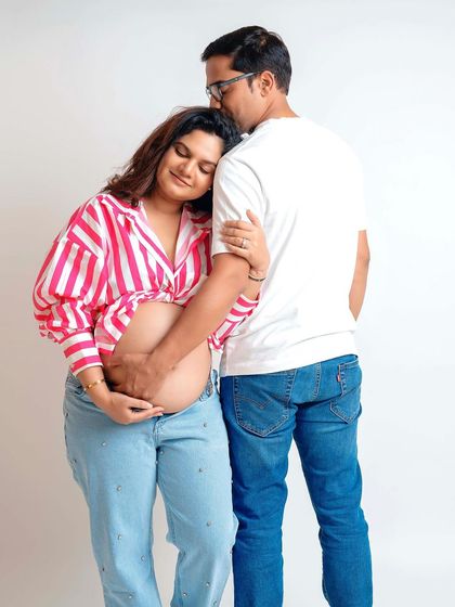 A casual and sweet moment between partners. The mom-to-be's striped shirt and jeans give this studio shot a relaxed, modern vibe.
