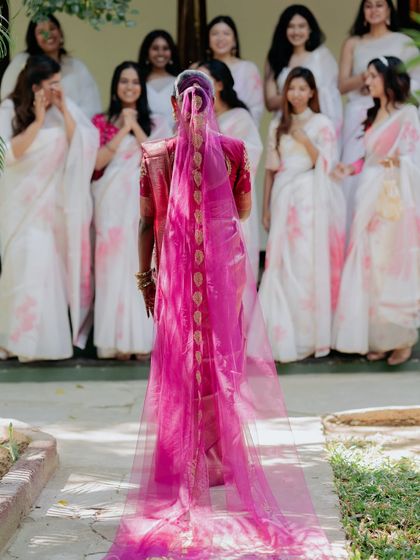 The bride's grand entrance, her face veiled, as her bridesmaids look on with emotion and excitement.