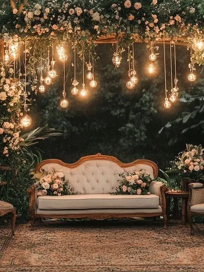 A cozy and rustic photo booth for a reception. The vintage sofa, floral arch, and hanging Edison bulbs create a warm and intimate spot for couple and guest photos.