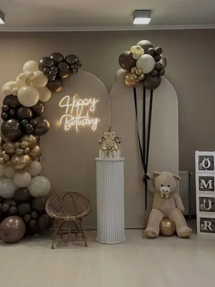 A gentle and modern teddy bear themed decoration. This setup uses a neutral color palette of brown, beige, and white balloons, with arched backdrops, a custom neon sign, and cute teddy bears, perfect for a first birthday or baby shower.
