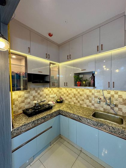 A corner view of a compact L-shaped kitchen. The design uses a mix of patterned backsplash tiles, light blue and grey cabinets, and profile handles for a unique look.