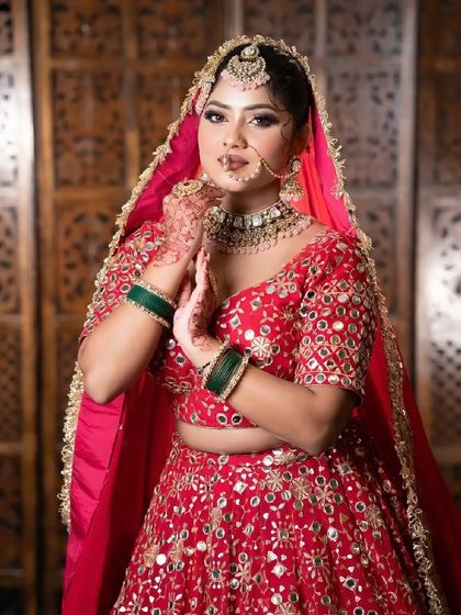 Another pose in the red mirror-work lehenga, showing the traditional 'namaste' gesture.