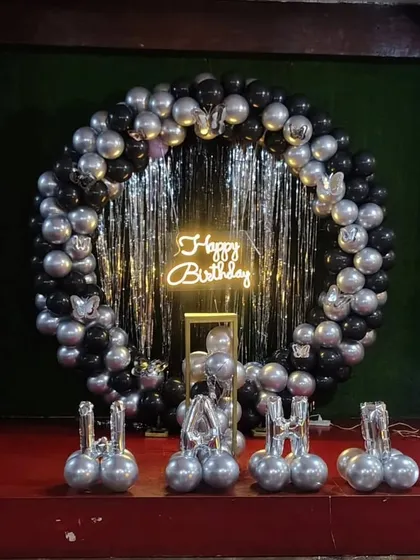 A black and silver balloon ring with a shimmering curtain and a neon sign, perfect for a teen's party.