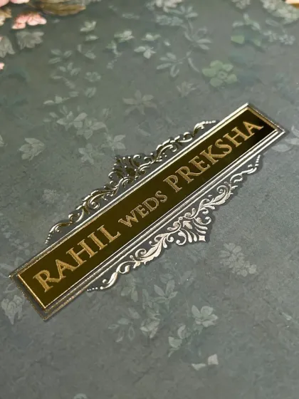 A close-up on the gold and silver foil nameplate, set against a subtle floral background, showcasing the blend of texture and shine.
