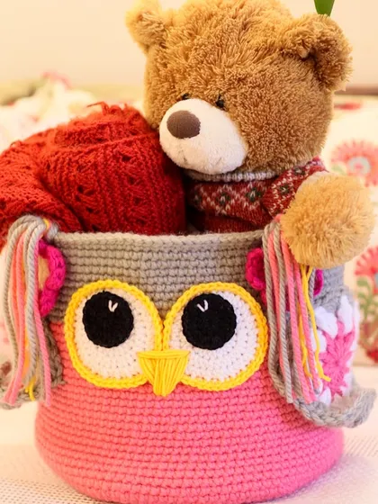 My bestselling Owlie Basket, peeking over with a teddy bear inside. Its sturdy construction ensures it can handle plenty of toys, blankets, or books.