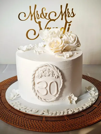 A pristine all-white cake for a 30th anniversary. The design features a custom "30" plaque and is elegantly decorated with white sugar flowers and a "Mr & Mrs" topper.