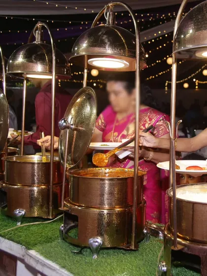 Guests enjoying a traditional Indian buffet served from elegant copper chafing dishes. This setup is perfect for weddings and large gatherings, ensuring the food stays warm and is served beautifully.