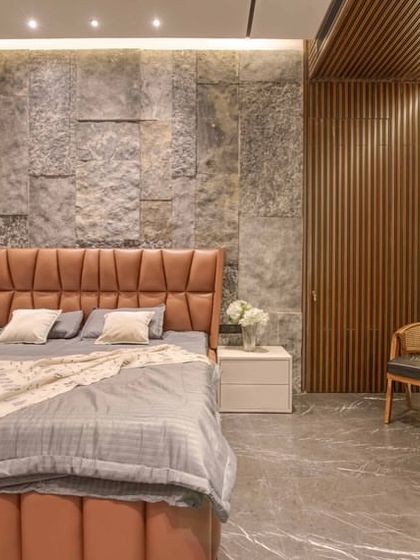 This bedroom combines a rustic stone accent wall with a warm, leather-upholstered bed. The vertical wooden slats of the hidden door add another layer of texture and interest.