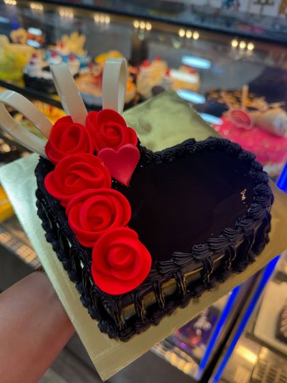 A dark chocolate heart-shaped cake with a basket-weave piping design. The red fondant roses and white chocolate ribbons add a touch of classic romance to this delicious cake.