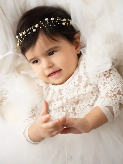 A close-up portrait of a baby girl in a delicate white lace dress and pearl headband. The details in this shot are just beautiful.