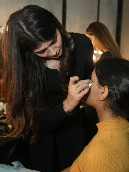 A student uses a cotton pad to perfect a model's eyeliner, demonstrating the attention to detail we instill in our artists.