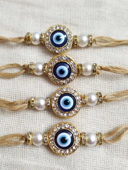 Protect your brother from 'buri nazar' with these classic evil eye rakhis. The design features a striking blue and white evil eye charm, surrounded by small crystals and set on a simple jute thread with pearl beads for an elegant touch.