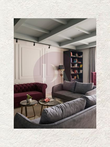 This view showcases the blend of classic and contemporary elements in one living room. A traditional burgundy Chesterfield sofa is paired with modern grey couches, all under a coffered ceiling that adds architectural interest.