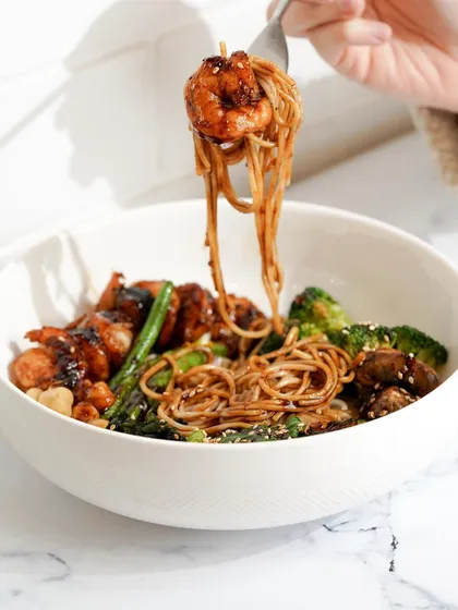 A dynamic shot of a prawn teriyaki noodle bowl, capturing the perfect noodle pull. This kind of action shot is highly engaging for social media and makes the dish look incredibly tempting.