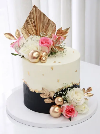 A tall and gorgeous cake for an engagement ceremony, featuring a black and white design with a fault line, gold leaf, and an arrangement of fresh flowers.