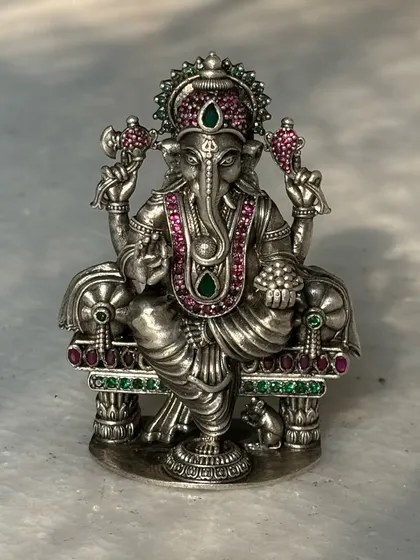 An antique-finish silver Ganesh murti, intricately detailed with pink and green stones. This piece combines traditional design with colourful accents, making it a unique addition to any collection.
