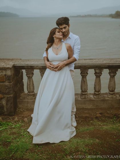 A full-length portrait of a couple in coordinated white outfits, sharing a quiet moment by the water. This showcases a classic, timeless pre-wedding photography style.