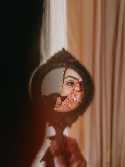 A creative shot reflecting the bride's eye in a mirror. This highlights the precision of the eye makeup, a key part of the overall bridal look.