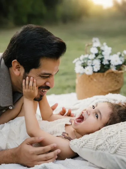 A father and daughter share a playful moment on a picnic blanket. The daughter's laughter is infectious in this candid outdoor shot.