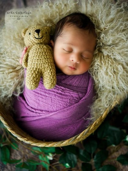 A sweet pose with a teddy bear tucked into the baby's arm, all wrapped in a lovely shade of purple.