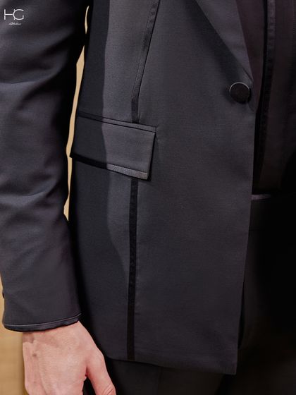 A detail shot of the all-black suit, focusing on the piped pocket and the sleek, continuous lines that give the jacket its extraordinary character.