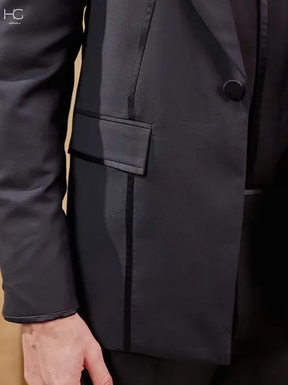 A detail shot of the all-black suit, focusing on the piped pocket and the sleek, continuous lines that give the jacket its extraordinary character.