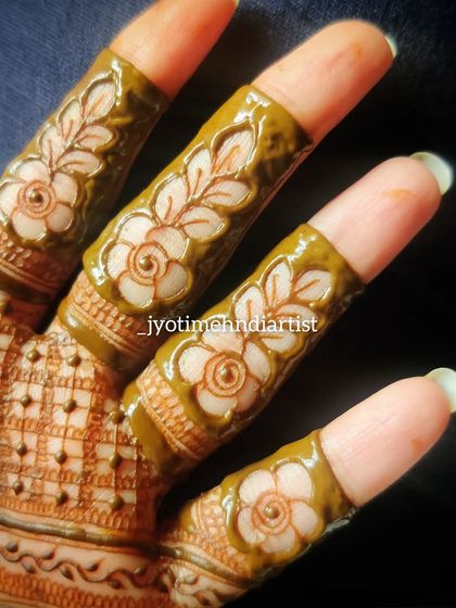 The completed floral cutwork finger design, with the dark henna paste creating a beautiful contrast.