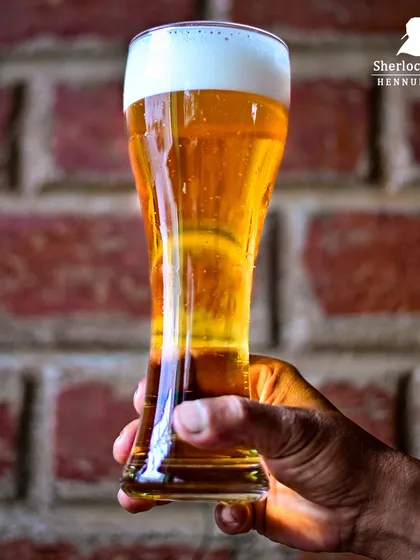 Holding up a glass of our golden brew against the classic brick wall. It's a simple pleasure that I love to provide for my guests.