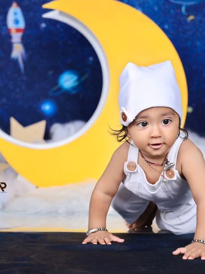 A baby astronaut crawls towards the camera, ready to explore the galaxy. The moon and stars props create a fun and imaginative setting.