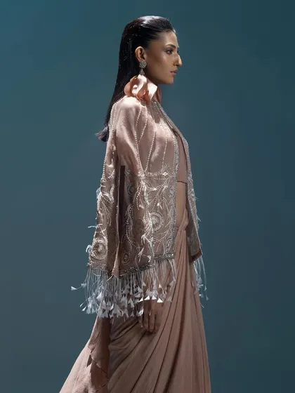 A modern draped saree in dusty rose, paired with an exquisitely embroidered and feathered cape, showcasing a high-fashion, avant-garde approach to ethnic wear.